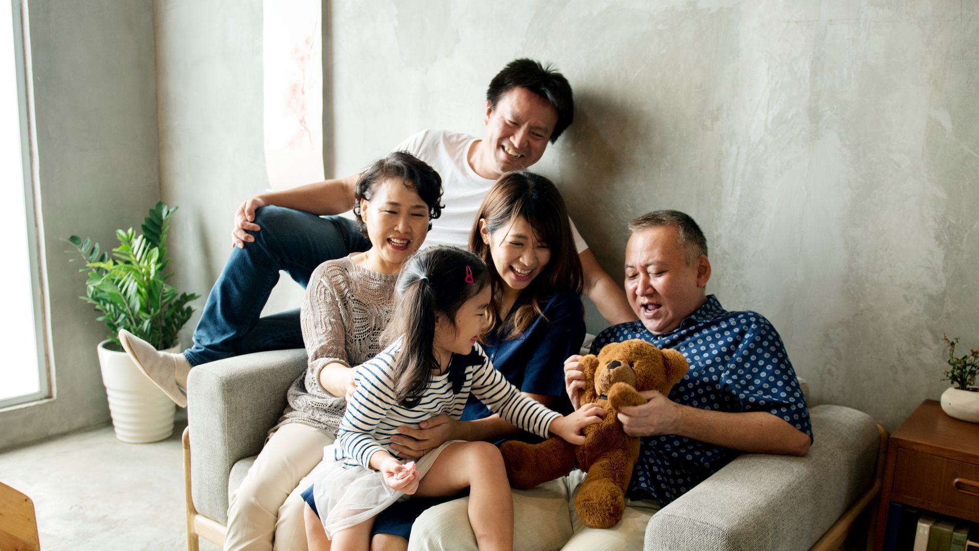 Family sitting together on a couch, smiling and holding a small dog in a bright living room.