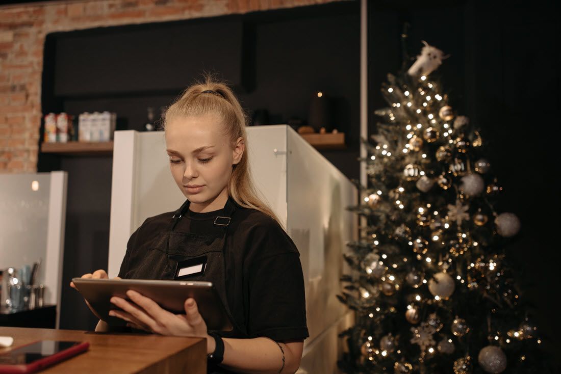 Woman holding a tablet at a café counter beside a lit Christmas tree