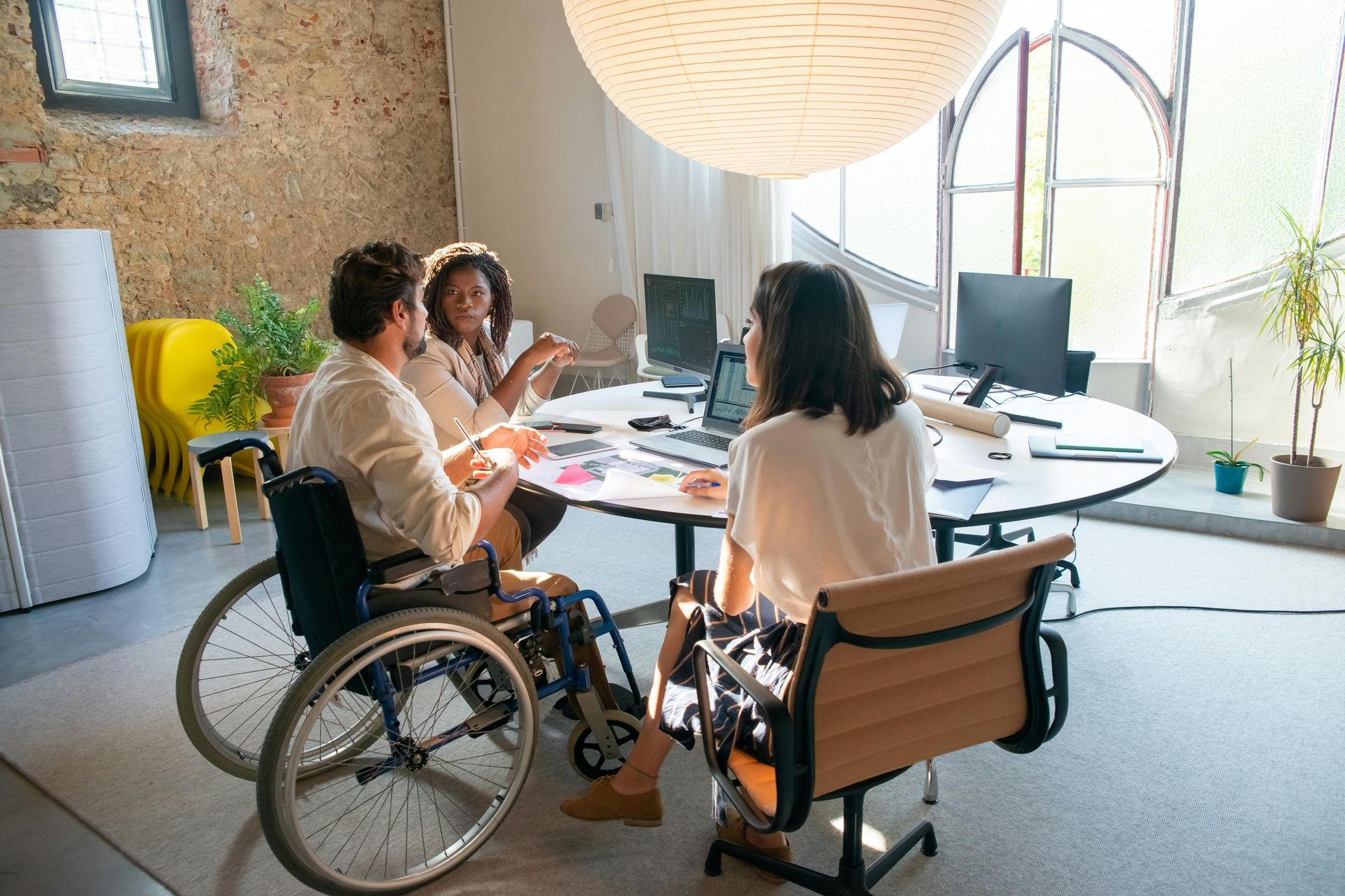 People meeting around a table in a bright office, with two wheelchairs visible.