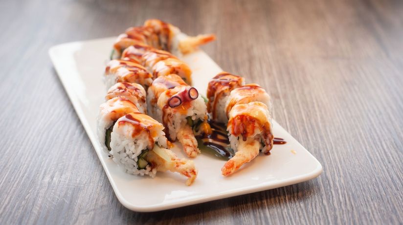 Sushi rolls drizzled with sauce on a white rectangular plate, served on a wooden table.