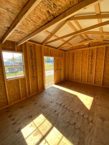 Empty framed room under construction with exposed wood walls, open windows, and sunlight on the floor