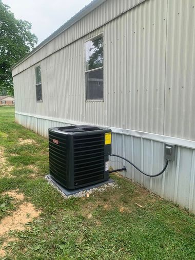 Exterior of a mobile building with a black air conditioner unit on a concrete pad beside it