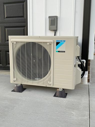 Beige outdoor air conditioner unit on concrete beside a house wall and dark door.