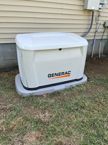 Beige portable generator on a concrete patio beside a stone house wall and window.