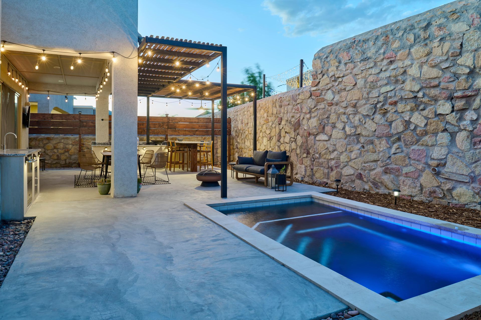 Backyard with a small pool, patio furniture under a pergola, and a stone wall.