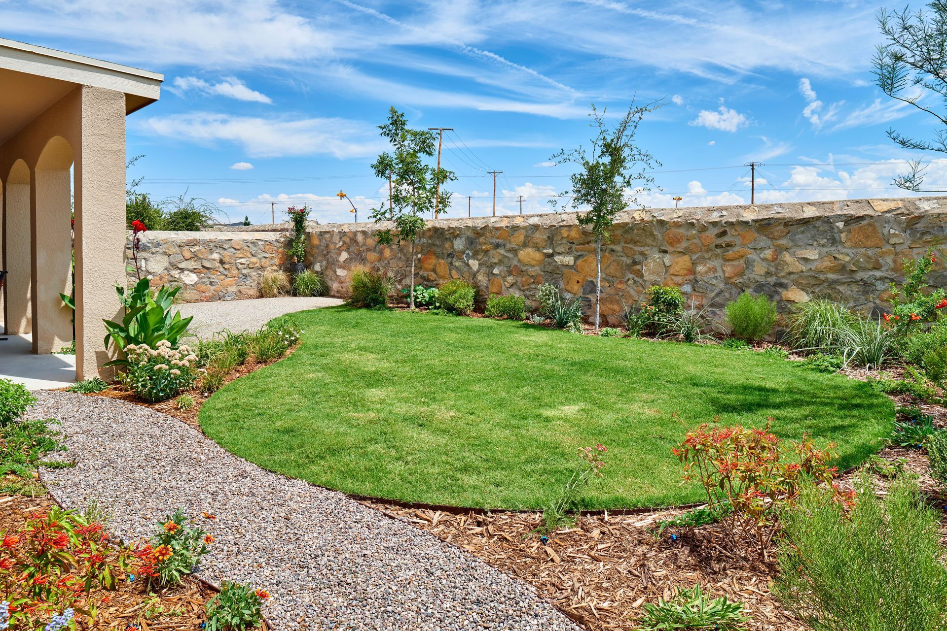 Well-manicured yard with grass, gravel path, and stone wall under blue sky.