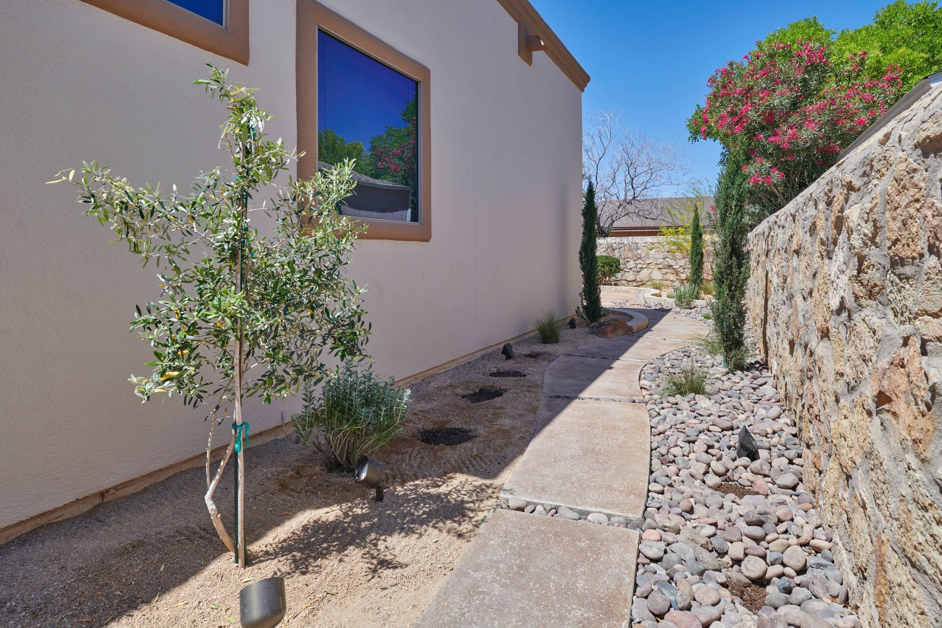 Side yard with a building, walkway, trees, and rock wall.