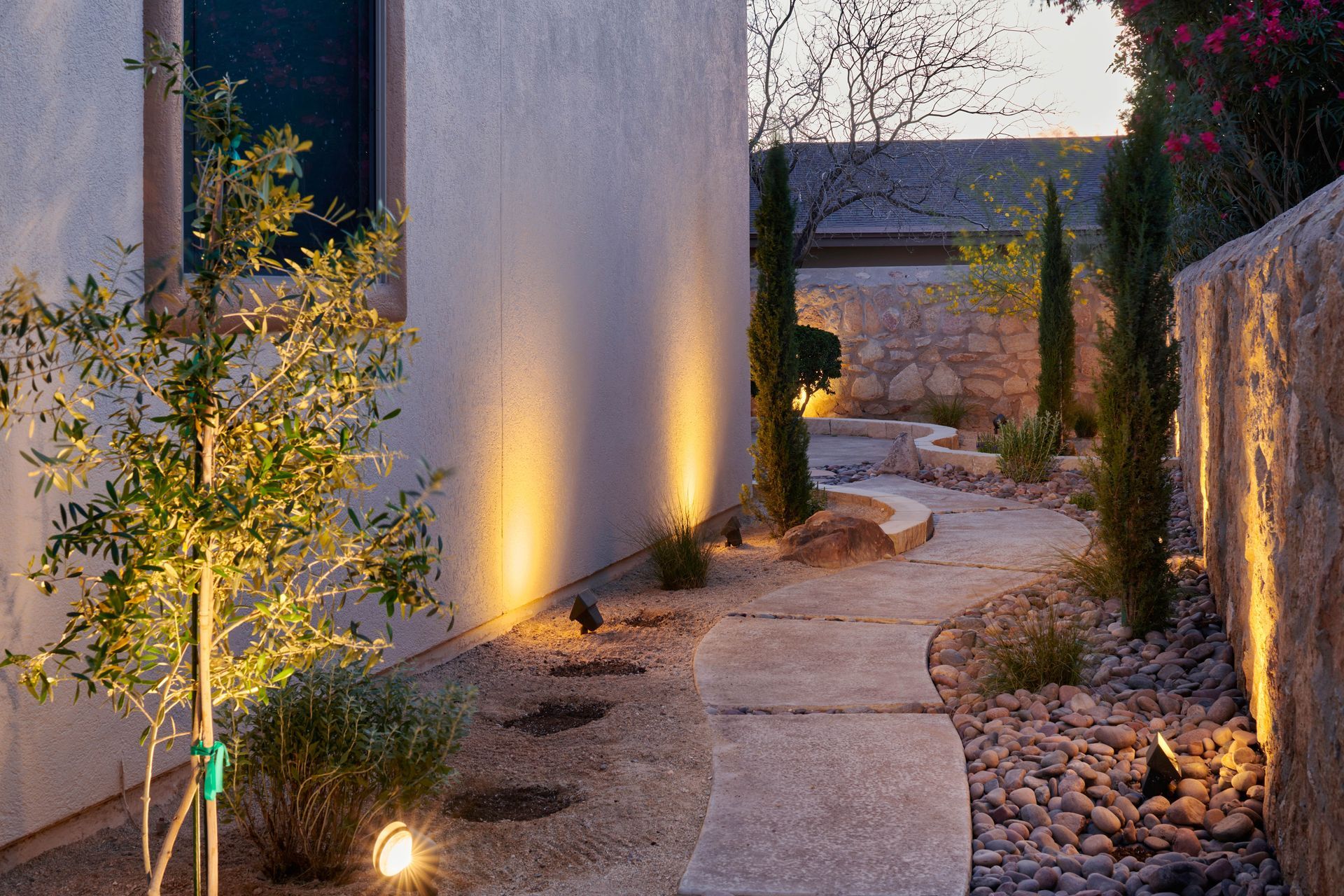 Pathway with landscape lighting, winding through a garden with trees and stone walls.