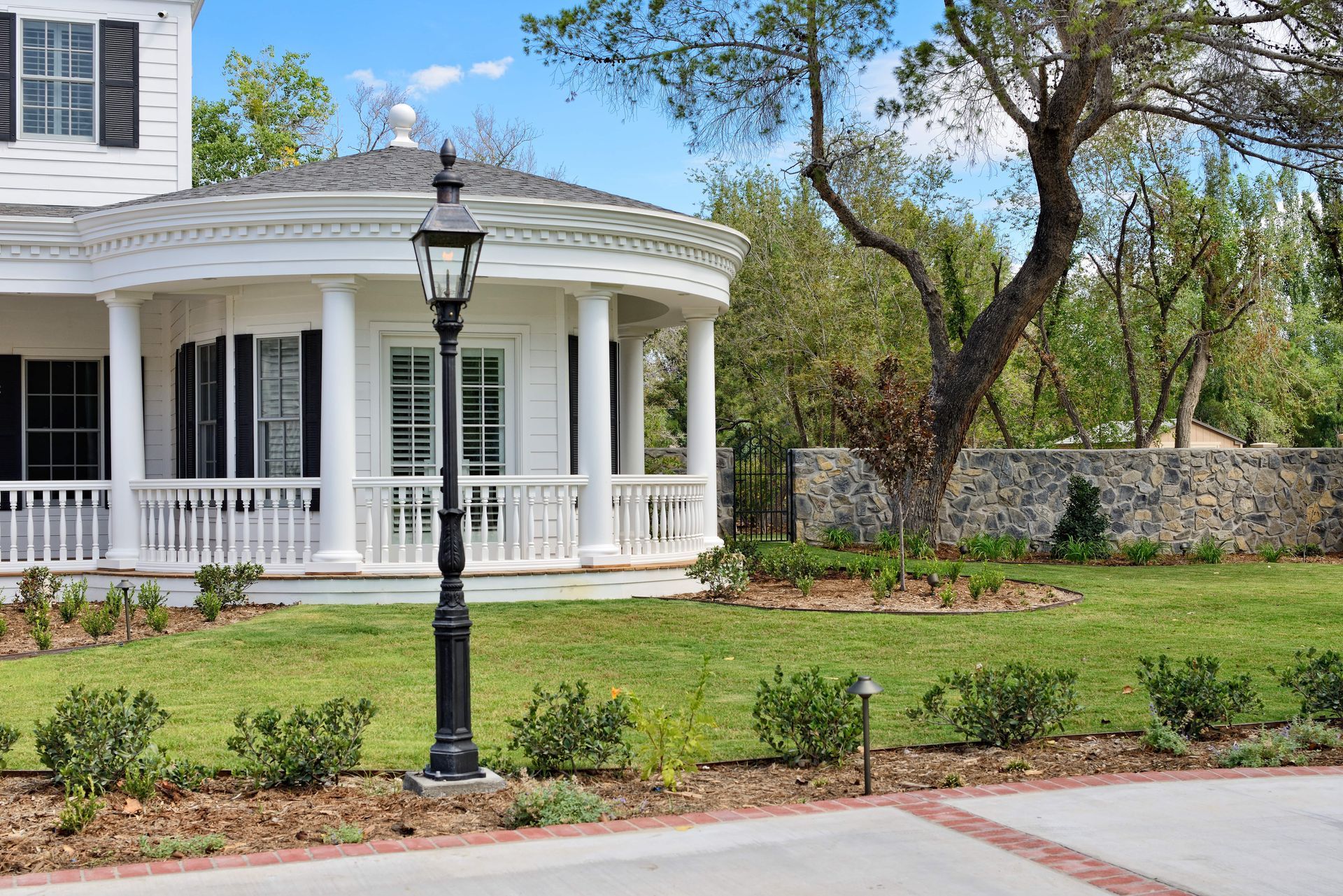White house with a curved porch, black lamppost, and manicured lawn.