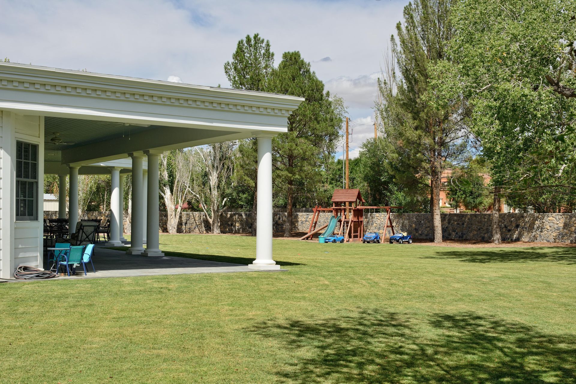 White porch with columns overlooking a backyard with green grass, a playset, and trees.