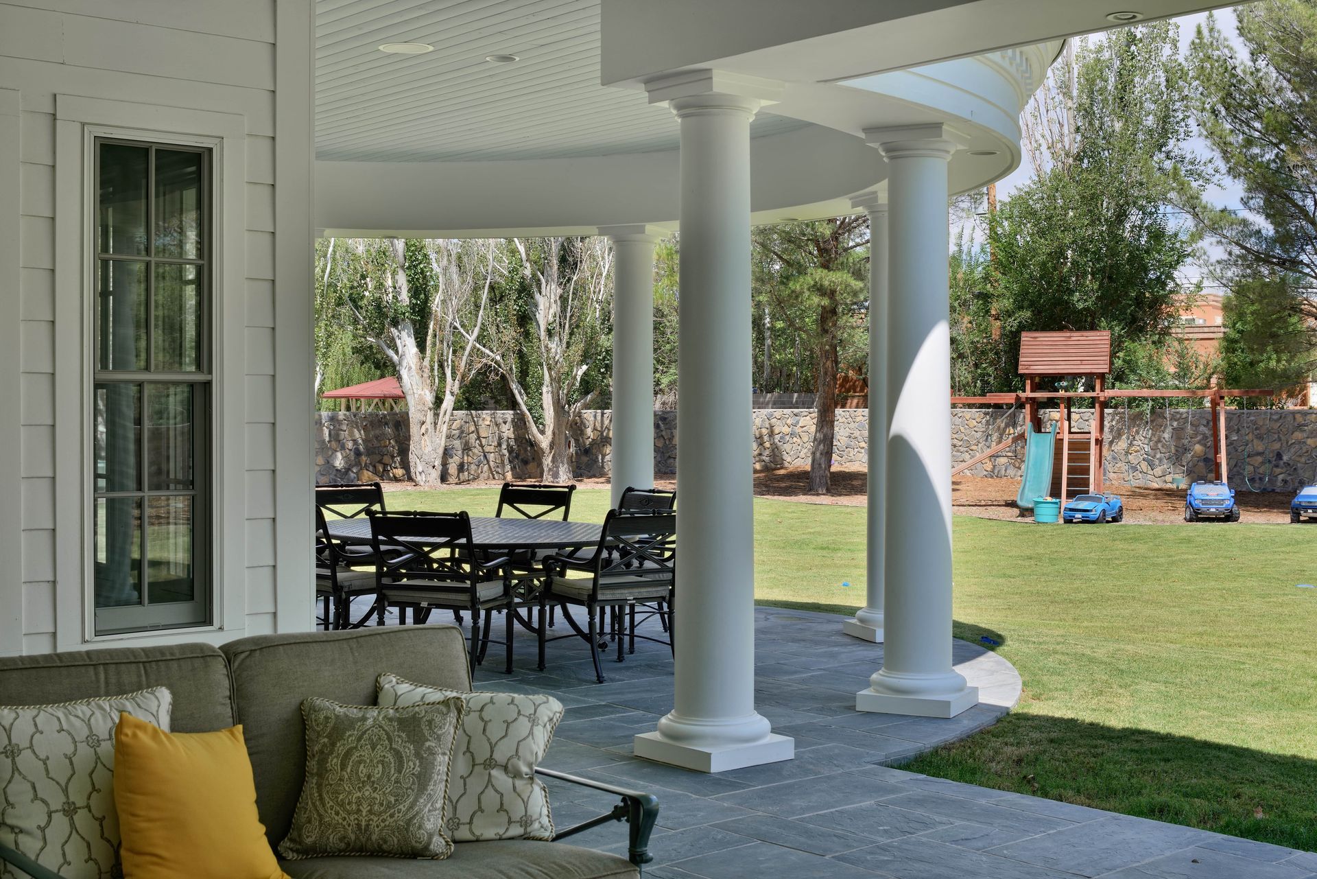 Covered patio with white columns and outdoor furniture overlooking a backyard with a playset.