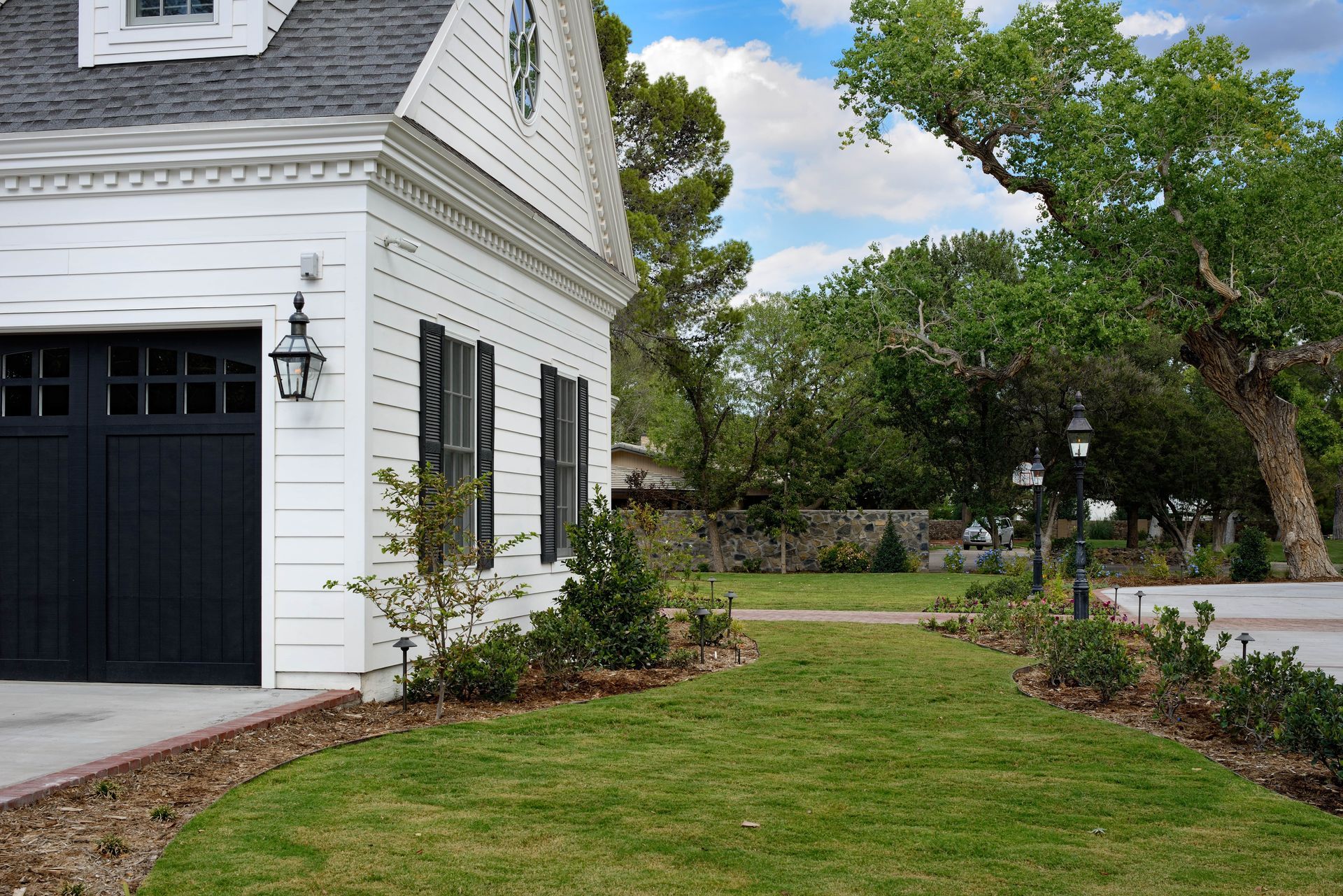 White house with black garage door, green lawn, trees, and blue sky.
