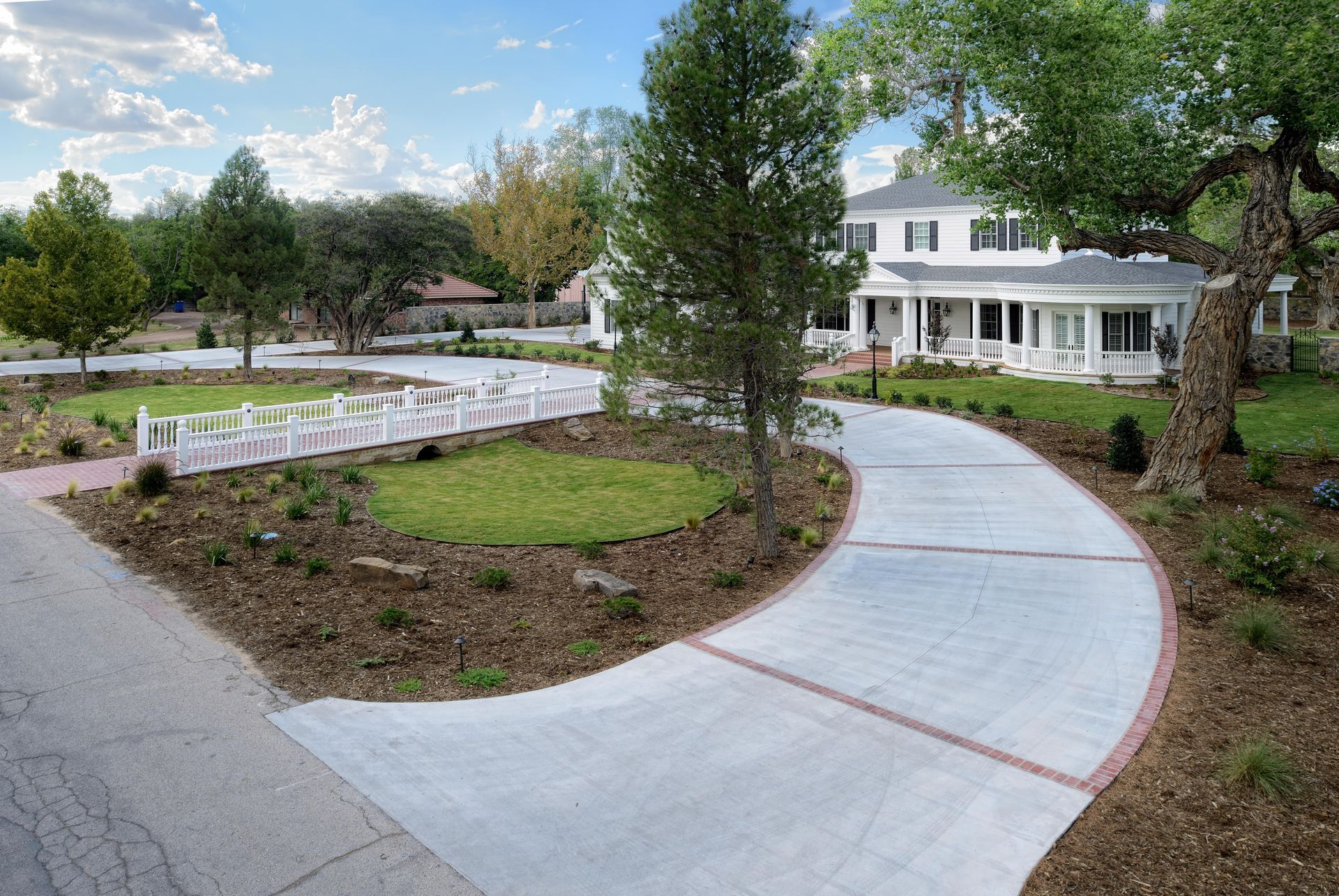 White colonial house with winding driveway and landscaping.