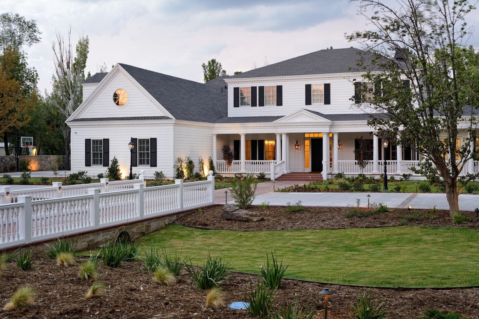 White house with black shutters, wraparound porch, and a bridge.