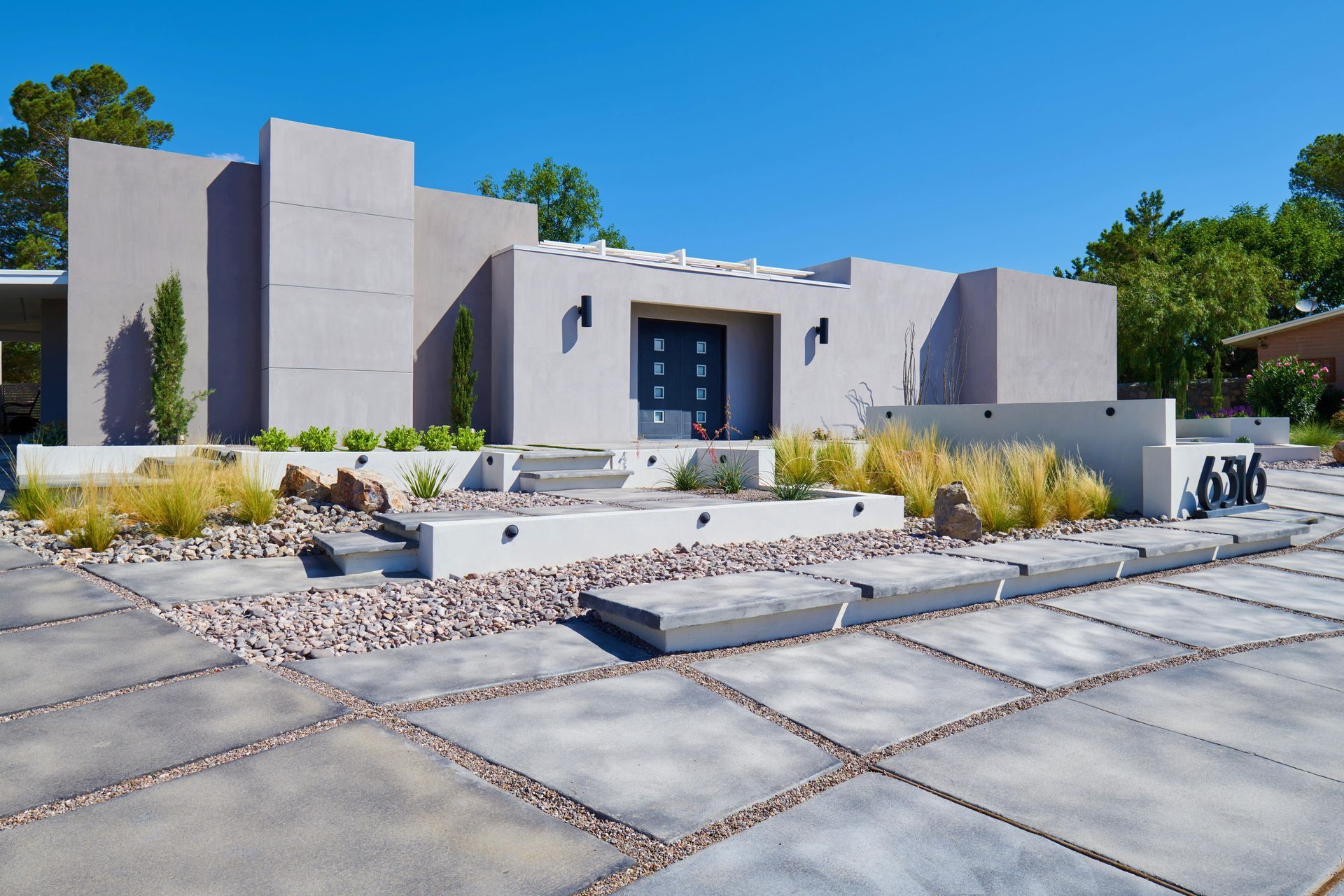 Modern, gray stucco home with concrete driveway and landscaping under a blue sky.