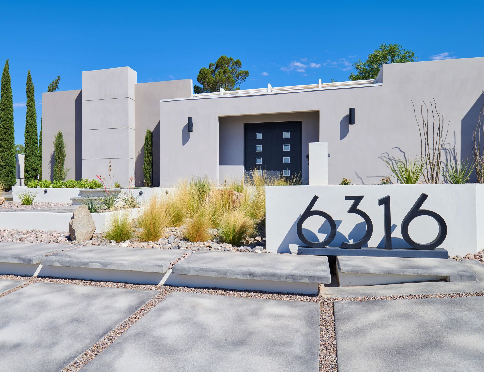 Modern house exterior with gray stucco walls, black door, and address numbers 