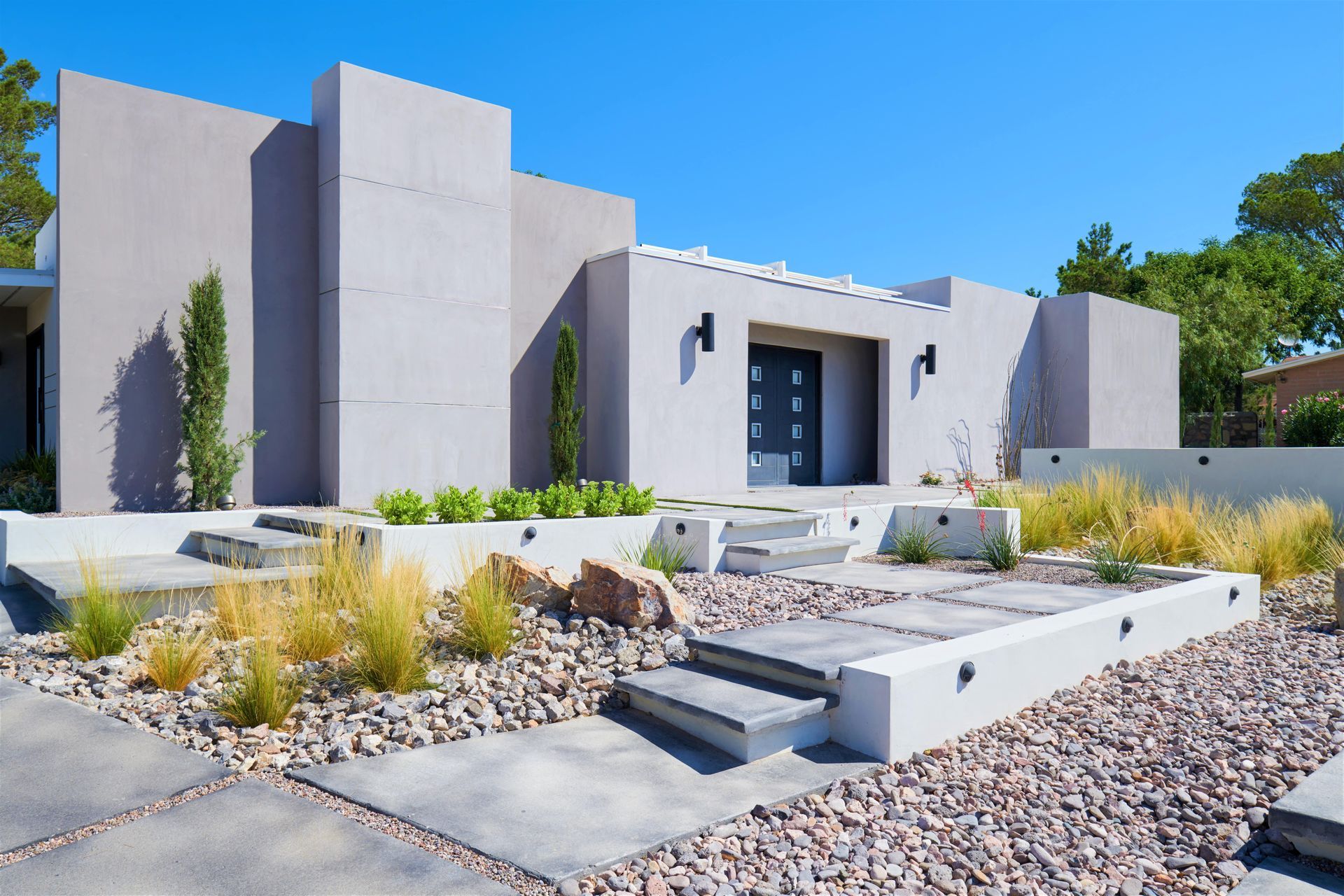Modern gray stucco home with stone landscaping and blue sky.