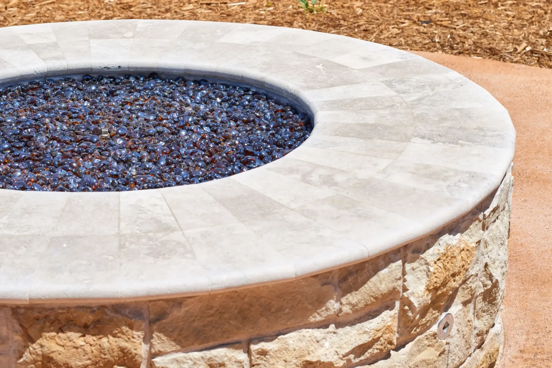 Circular stone fire pit filled with blue glass.