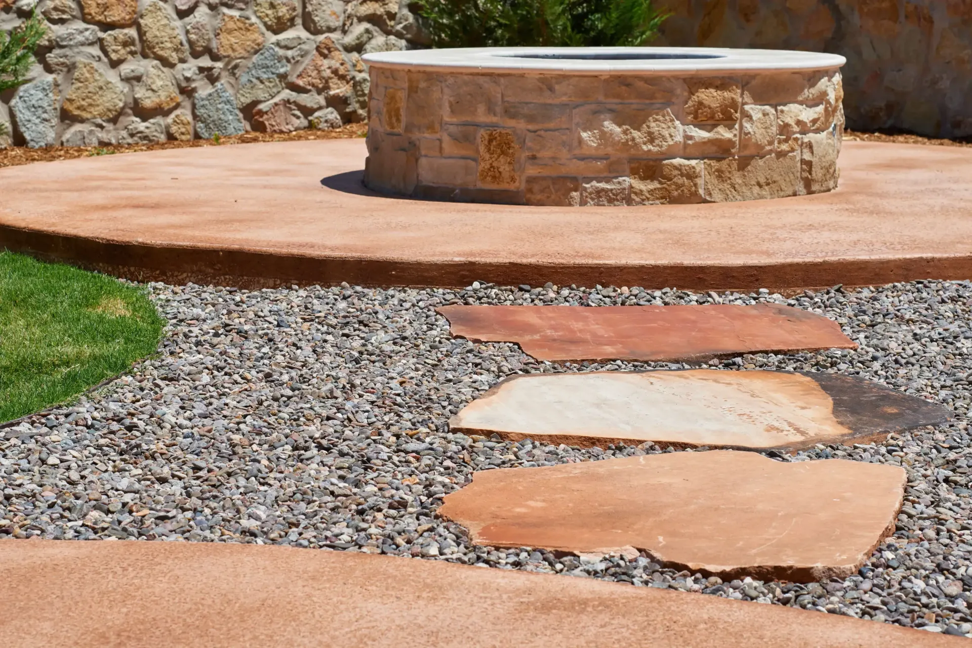 Stone fire pit on a concrete patio with stepping stones and gravel path.