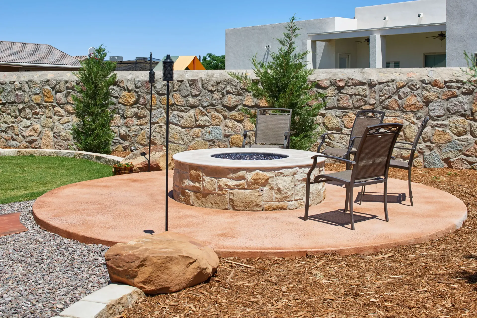 Outdoor patio with a stone fire pit, chairs, and surrounding landscaping.