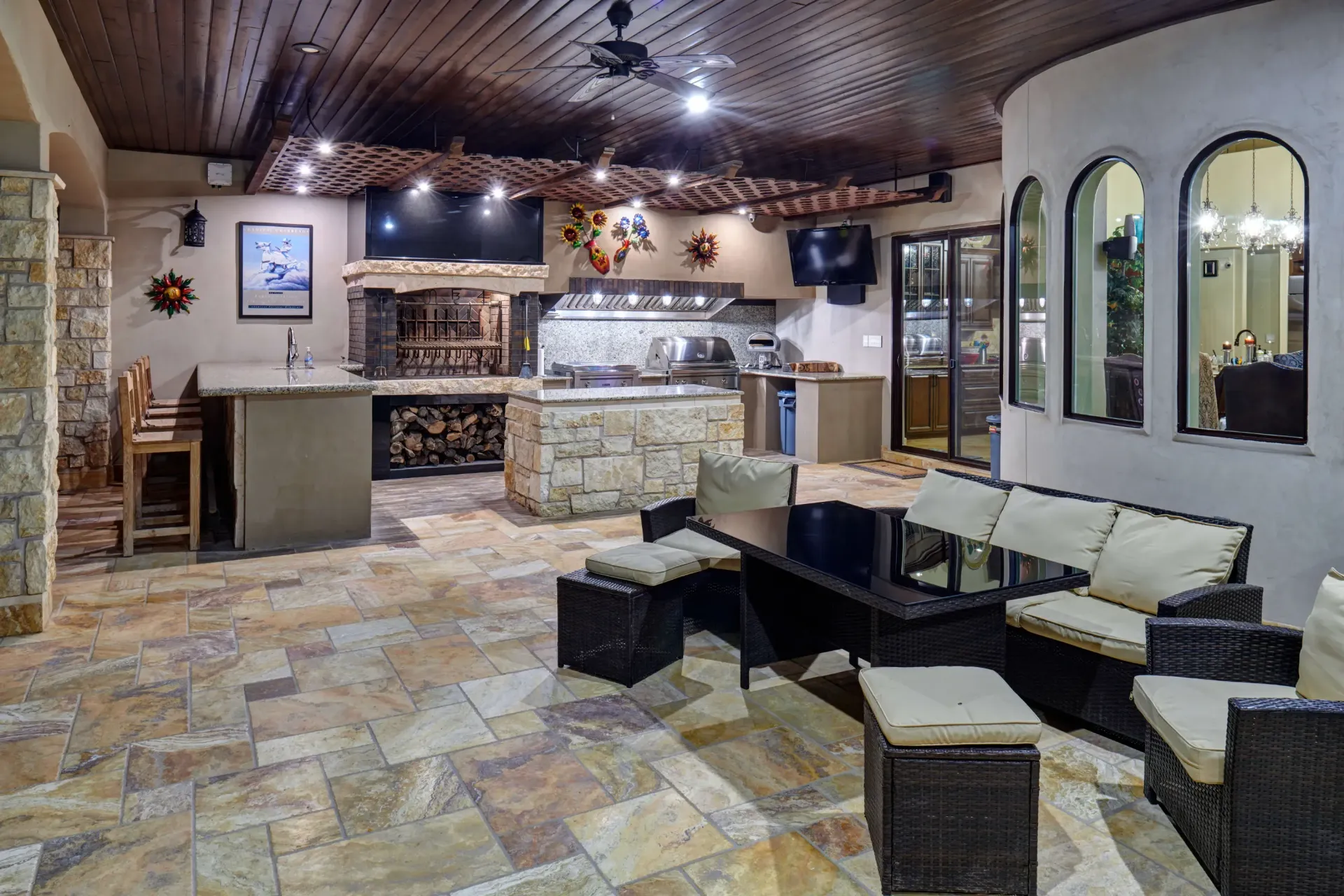 Patio with outdoor kitchen, seating area, stone counters, wooden ceiling, and arched windows.