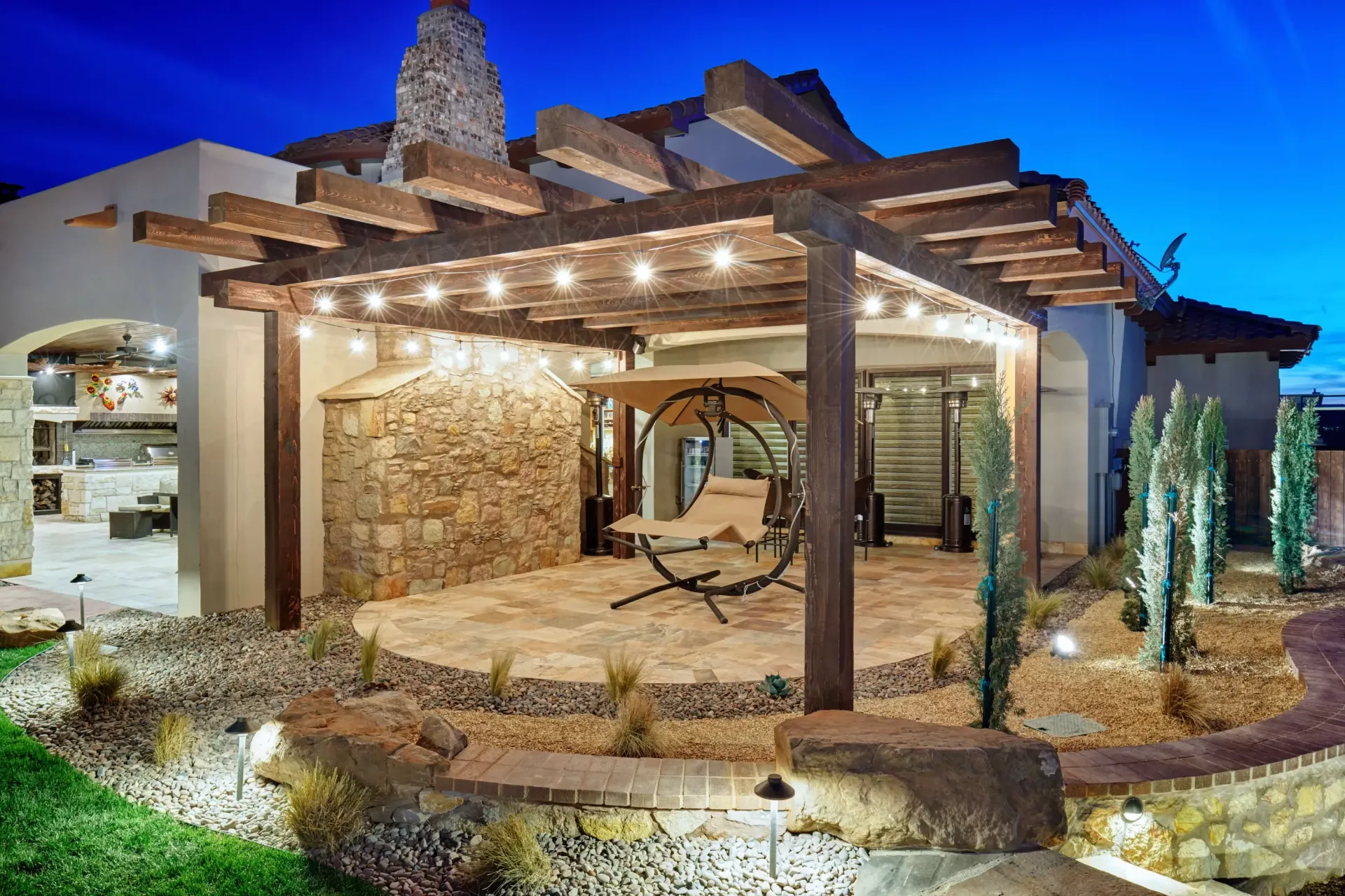 Patio with a pergola, string lights, and a hanging swing; night setting.