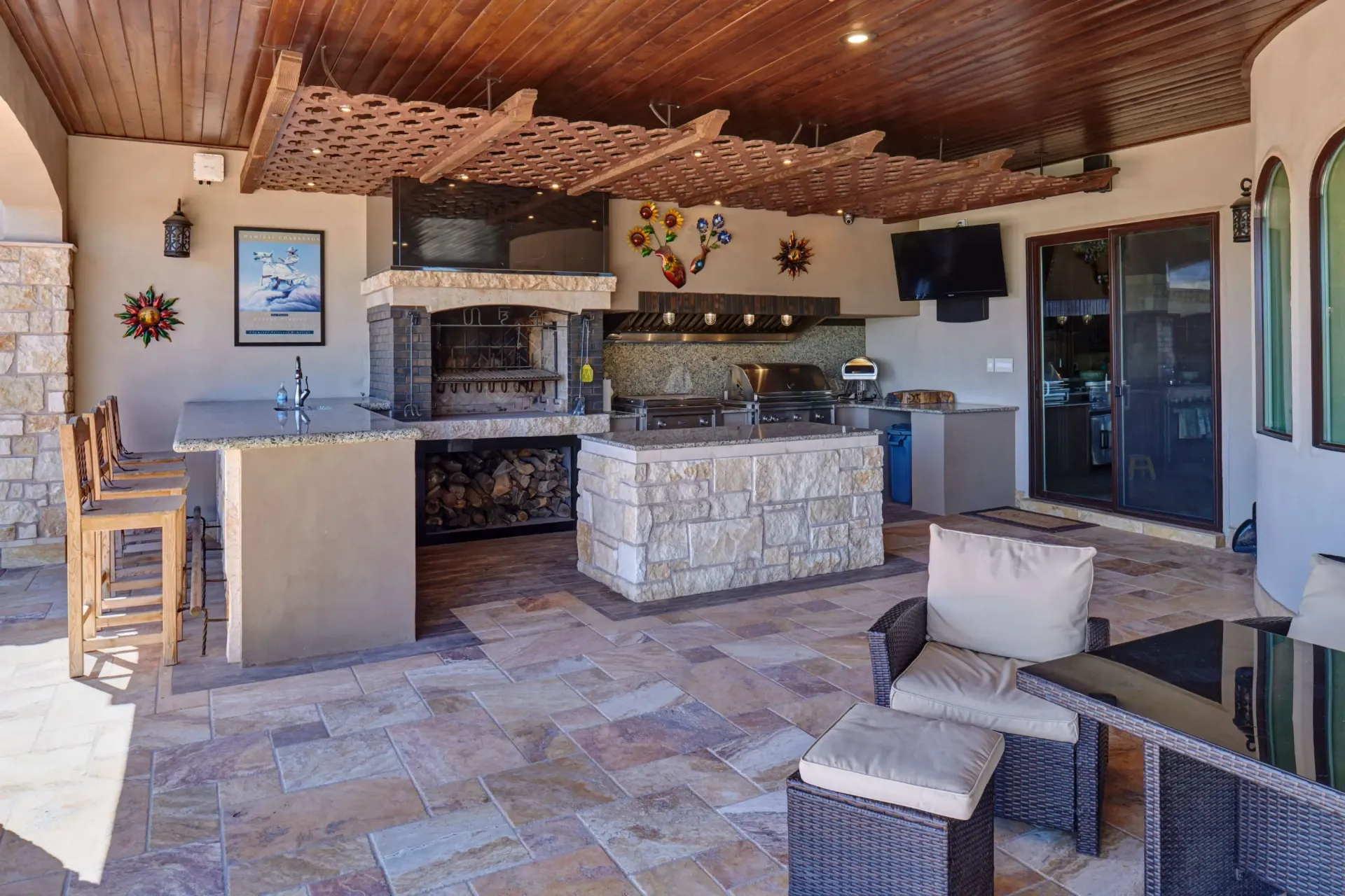 Outdoor kitchen with stone counters, a grill, seating, and a TV.