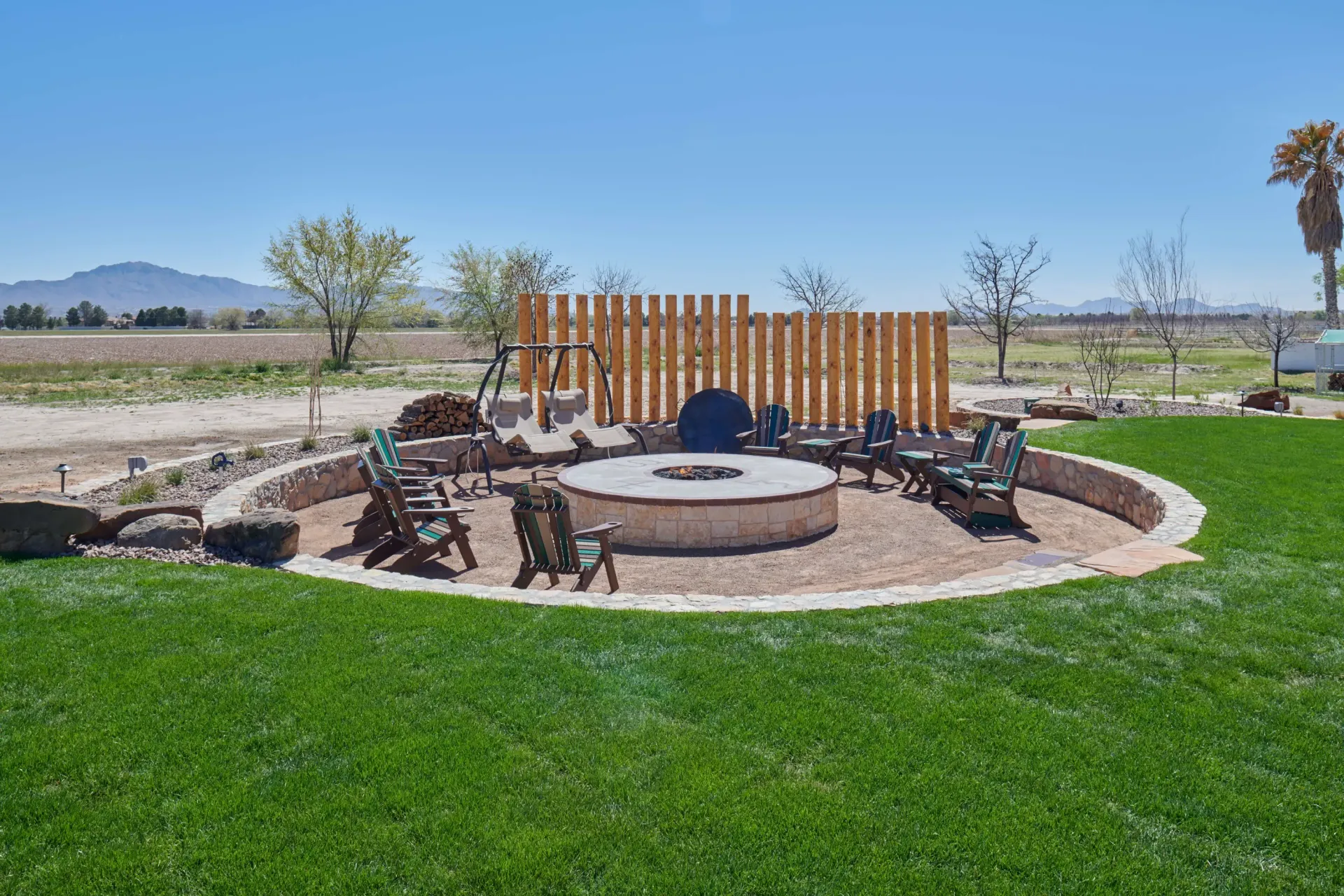 Fire pit area with seating, wooden fence, surrounded by gravel and green grass.