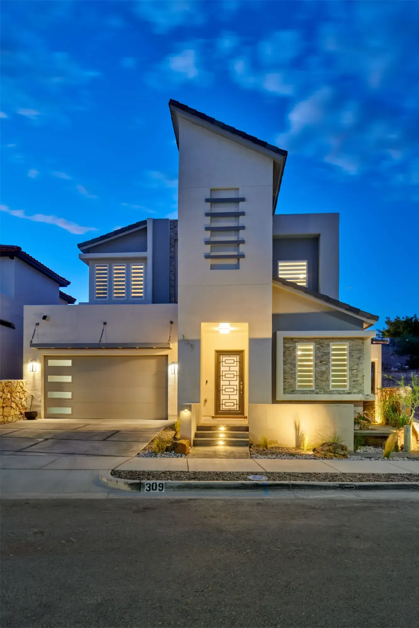 Modern two-story house with light gray and white exterior. Features a sloped roof, garage, and decorative front door.