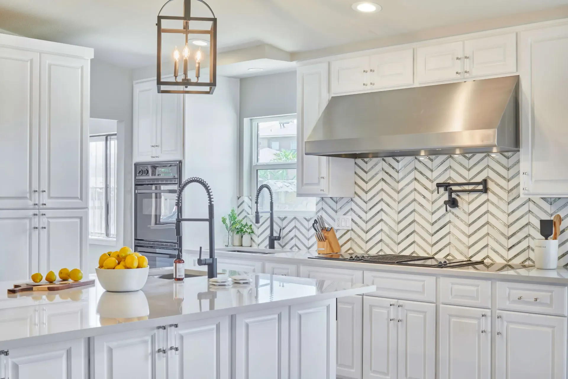 White kitchen with island, herringbone backsplash, stainless steel hood, and black faucets.