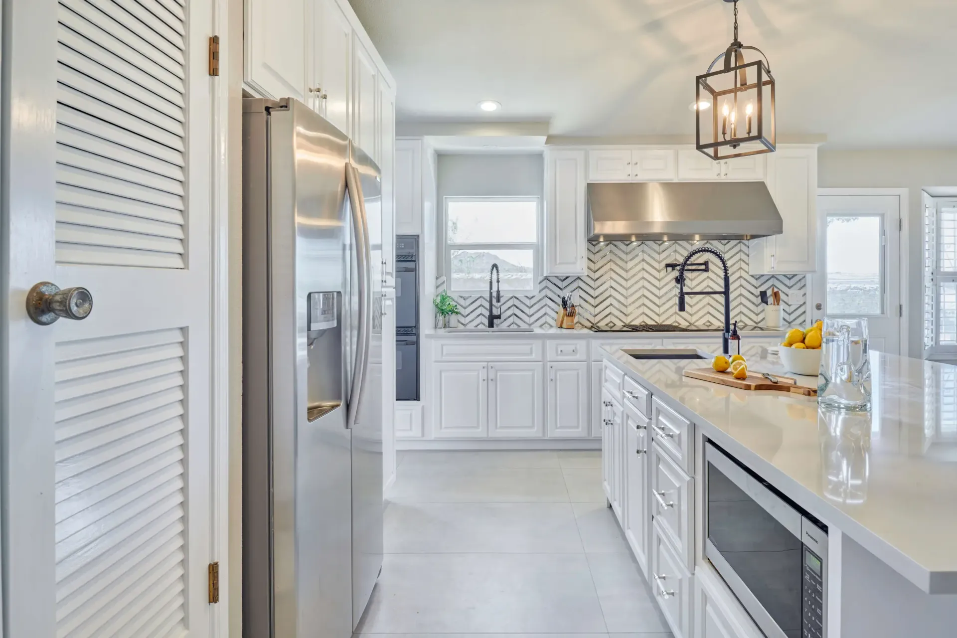 White kitchen with stainless steel appliances, white cabinets, and island with a microwave.