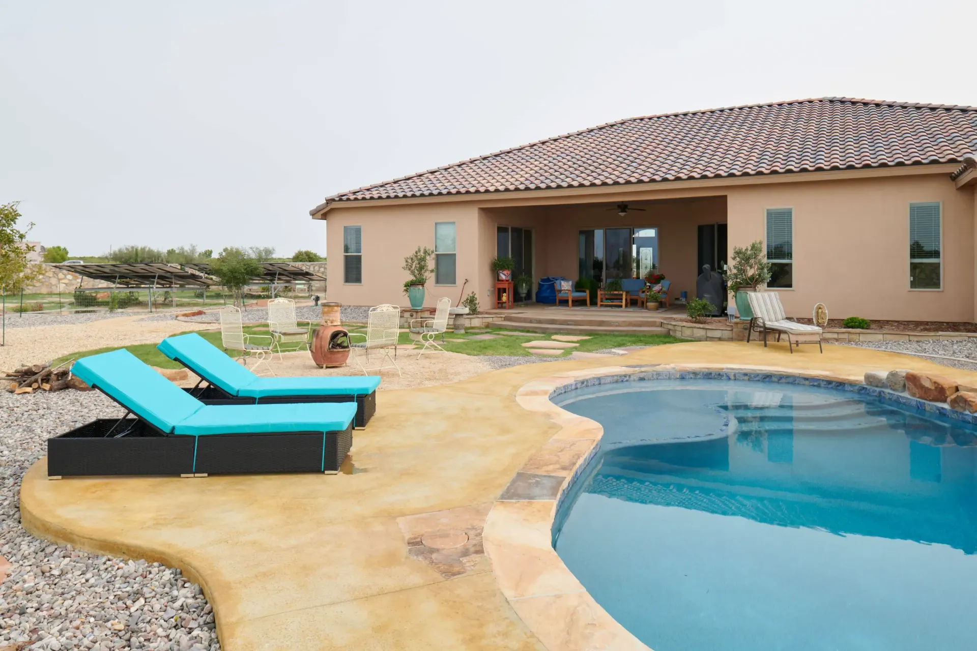Backyard with pool, lounge chairs, and house with terracotta roof.