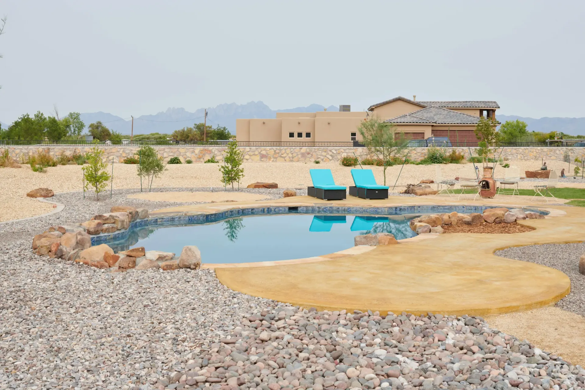 Pool with turquoise water and lounge chairs, surrounded by rocks and a beige patio. Desert landscape in background.