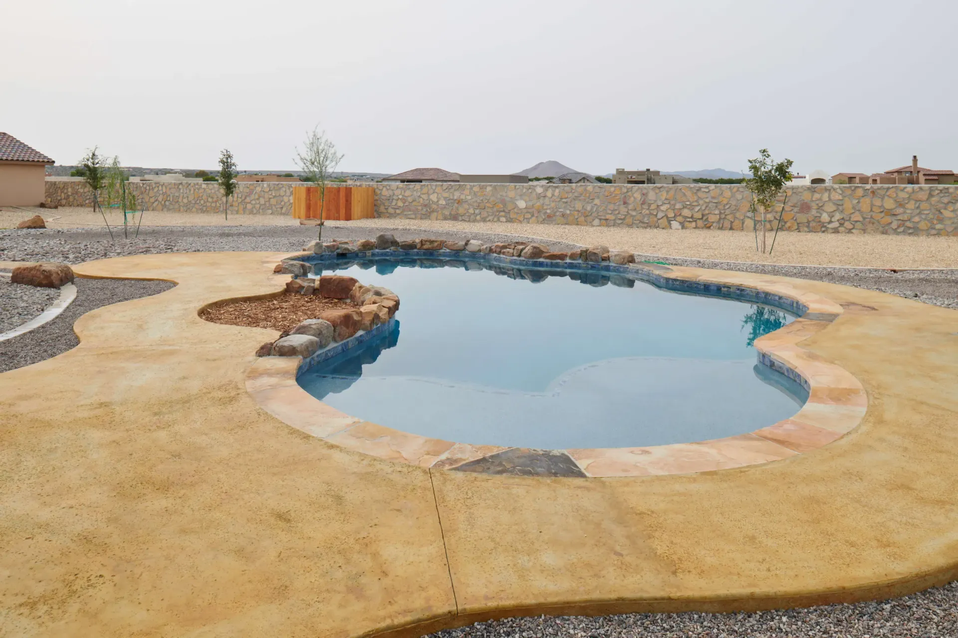 A kidney-shaped swimming pool with tan concrete surround in a desert backyard.