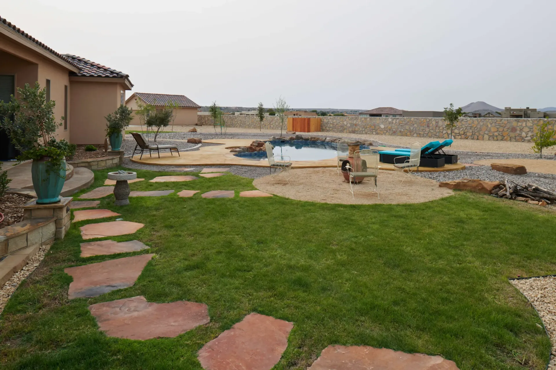 Lawn and stone path lead to a backyard with a pool, lounge chairs, and desert landscaping.