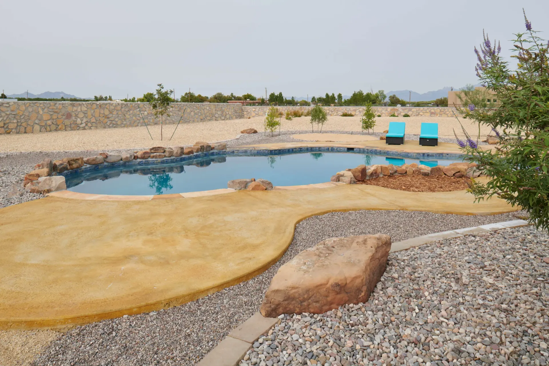 Swimming pool surrounded by stone and gravel landscaping; blue lounge chairs in the background.