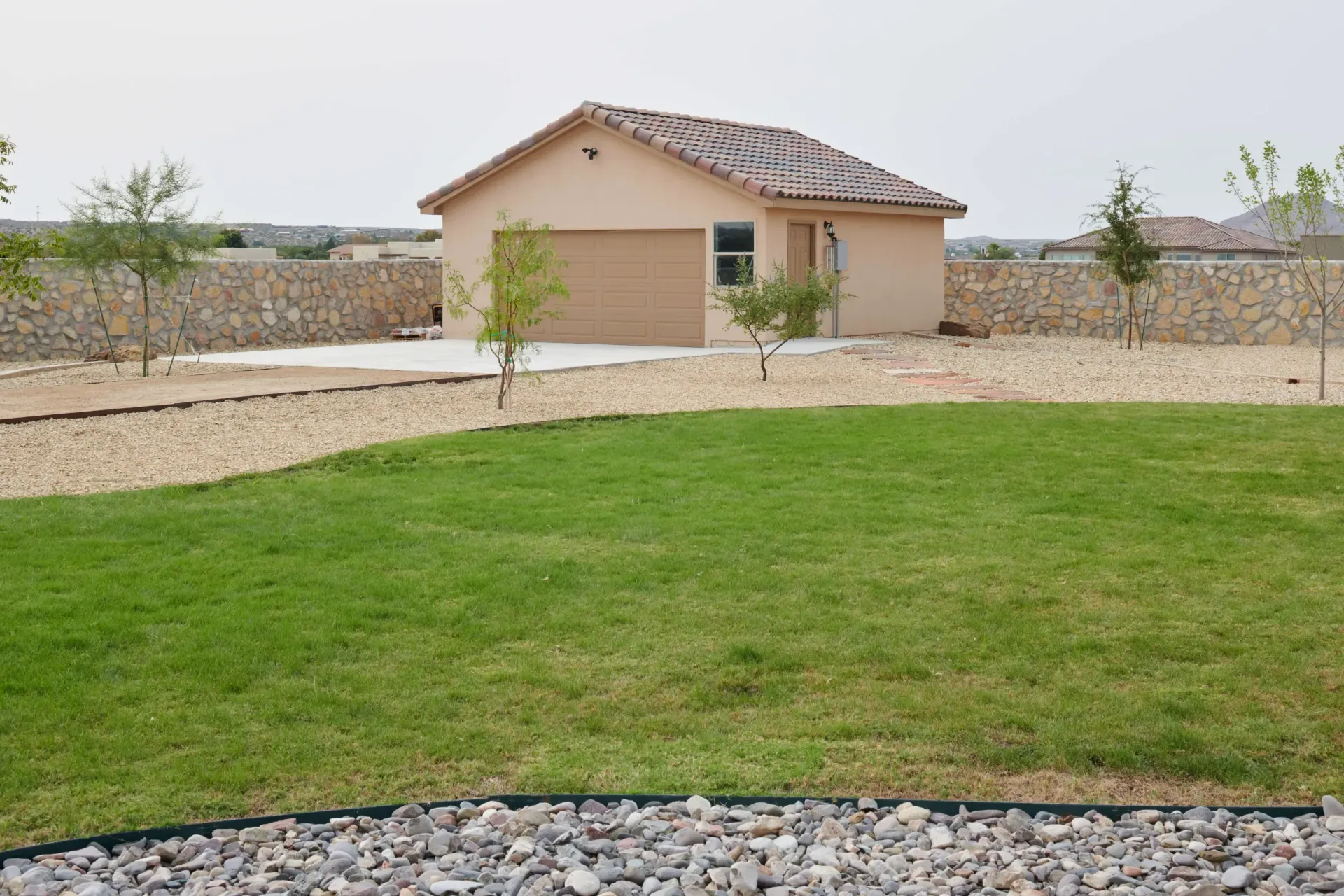 Tan stucco garage in a gravel yard, with a green lawn in the foreground.