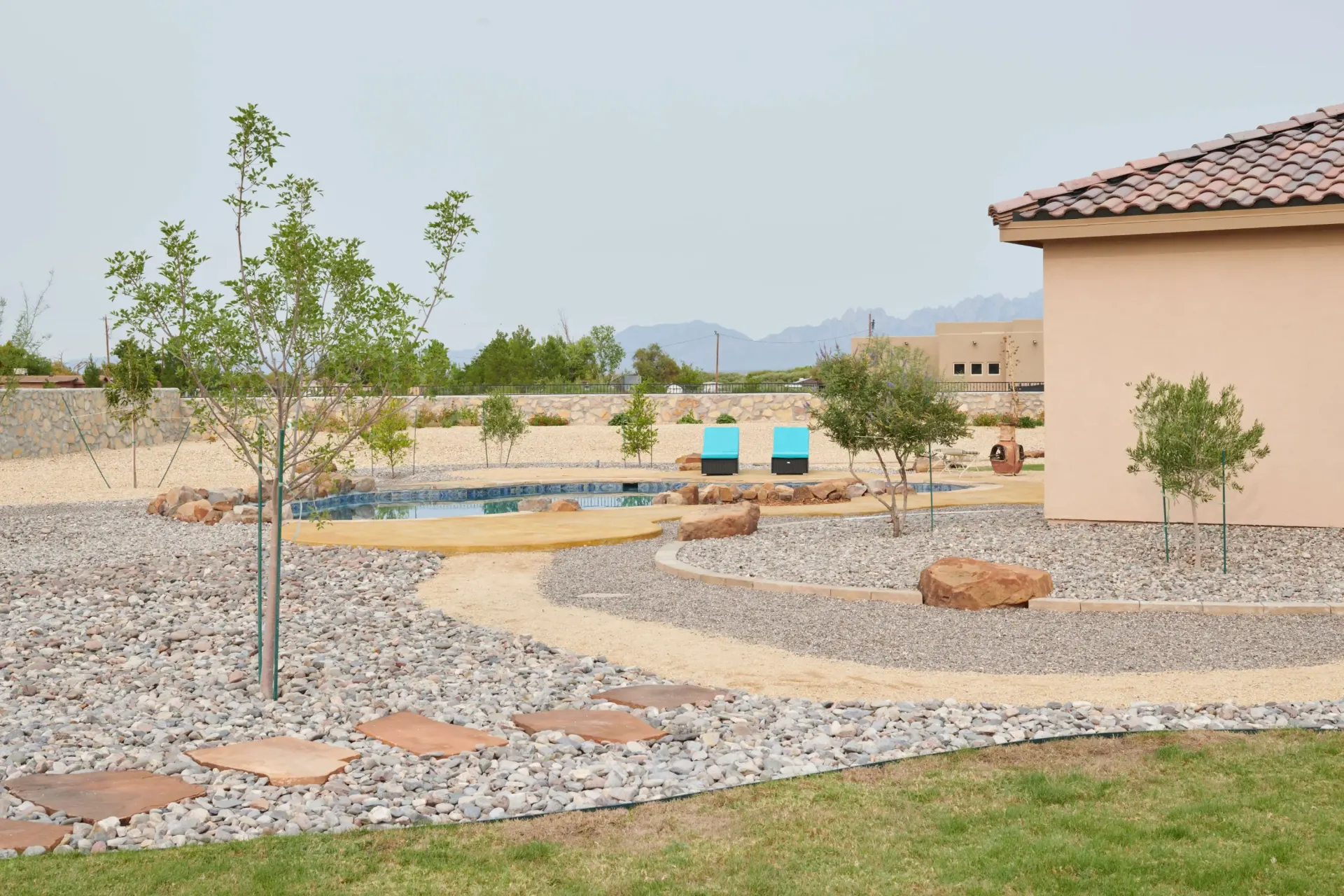 A backyard with a pool, gravel landscaping, a winding stone path, and a building with a tile roof.