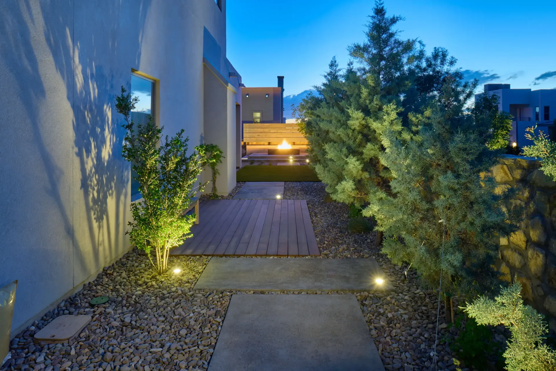 Lit pathway between a building and landscaping at dusk.