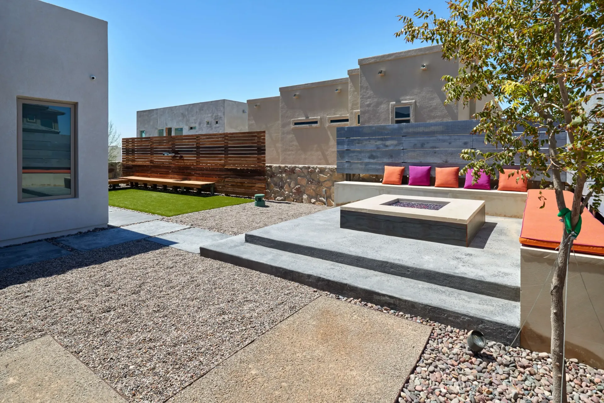 Outdoor patio with fire pit, seating, and landscaping in sunny setting.