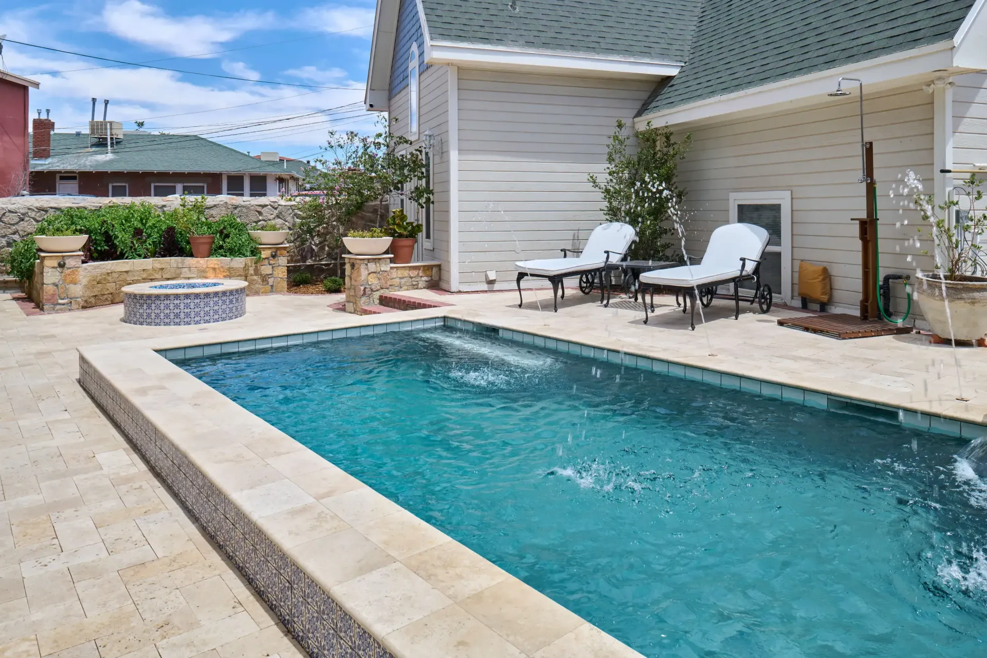 Rectangular pool with turquoise water, surrounded by beige paving. Lounge chairs sit nearby. Sunny outdoor setting.