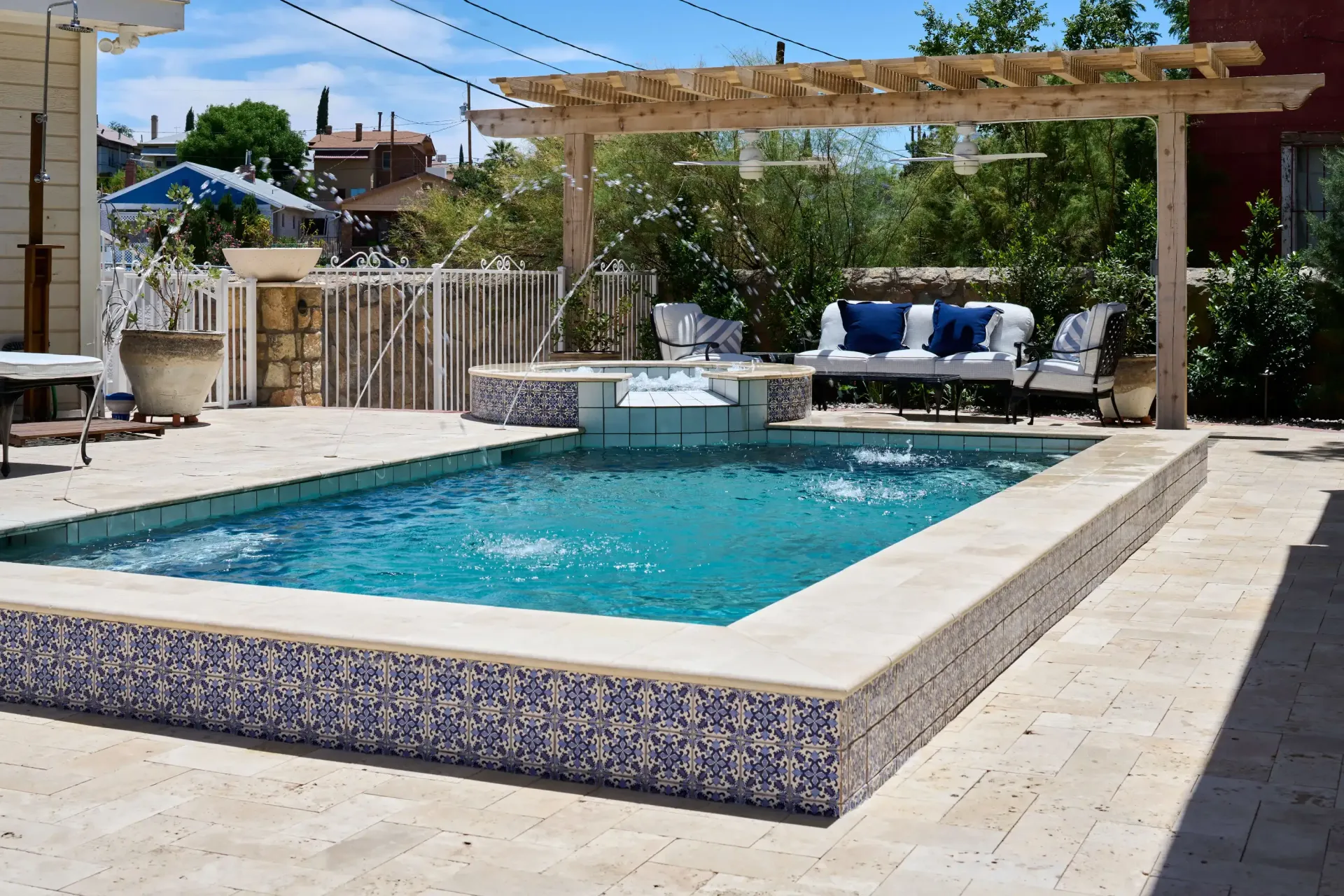 Pool with blue water and tiled edges, pergola, and white seating area outdoors.