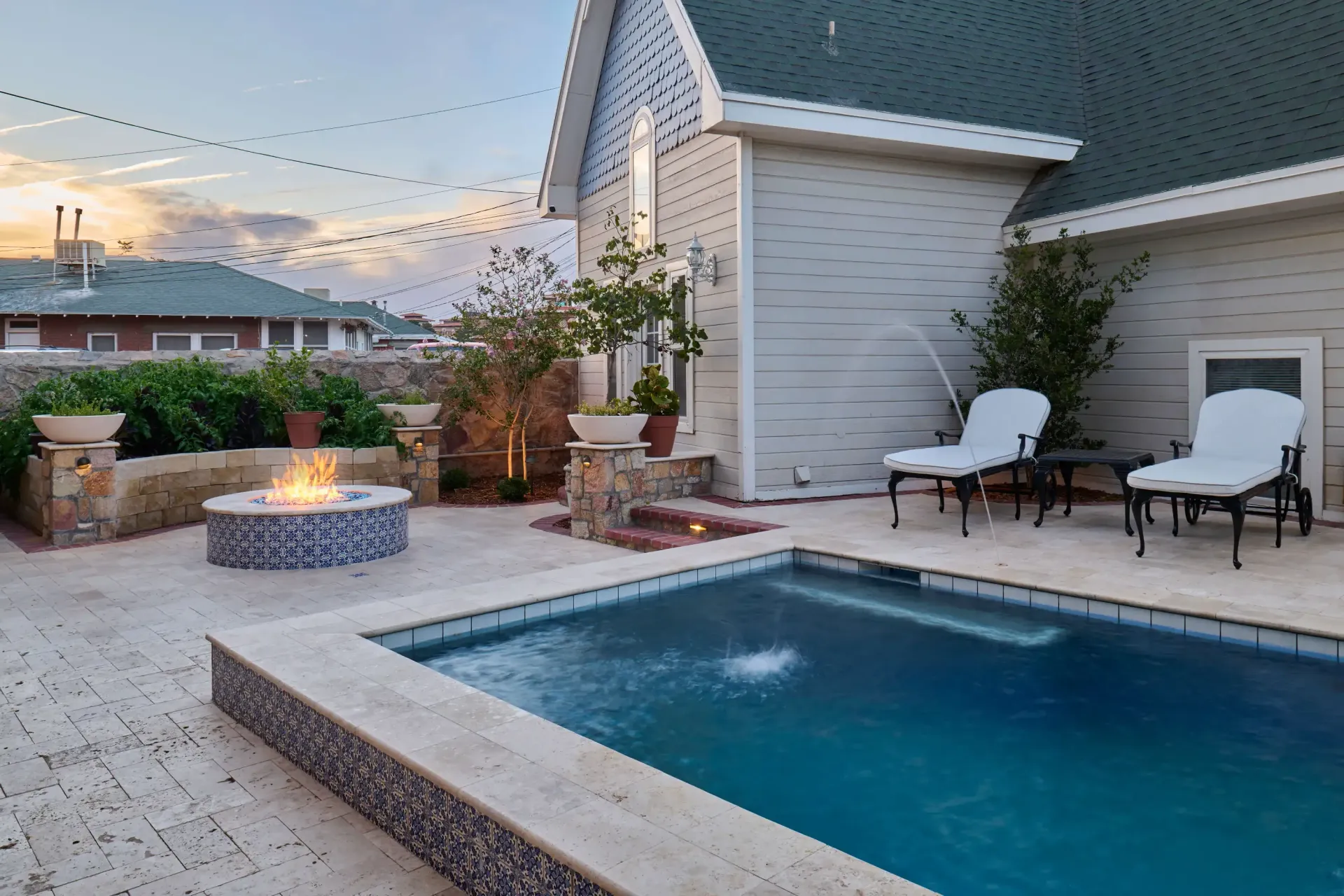 Backyard with a pool, fire pit, and lounge chairs. Evening scene with string lights and a house in the background.
