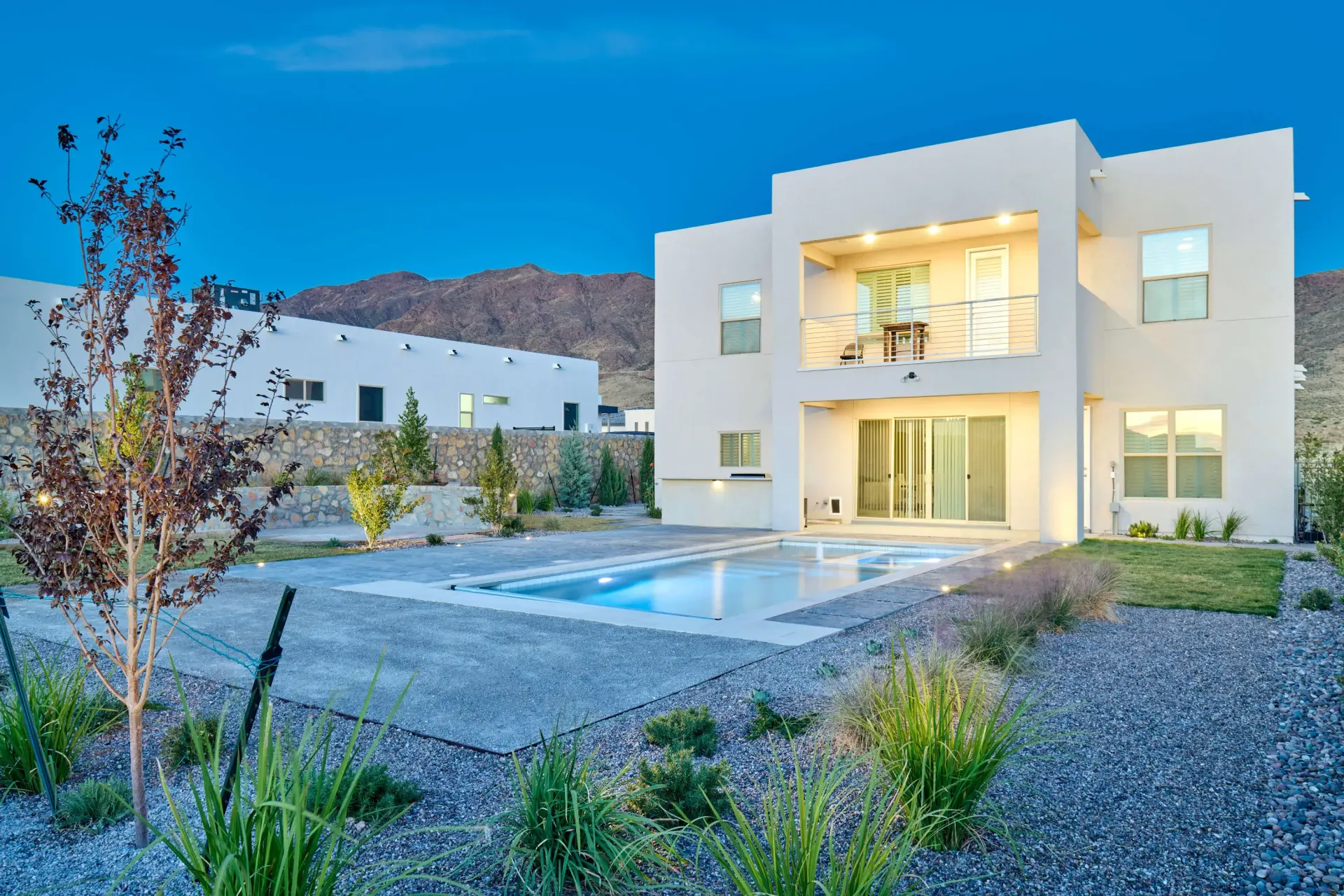 Modern two-story house with a pool in a desert landscape. Blue twilight sky.