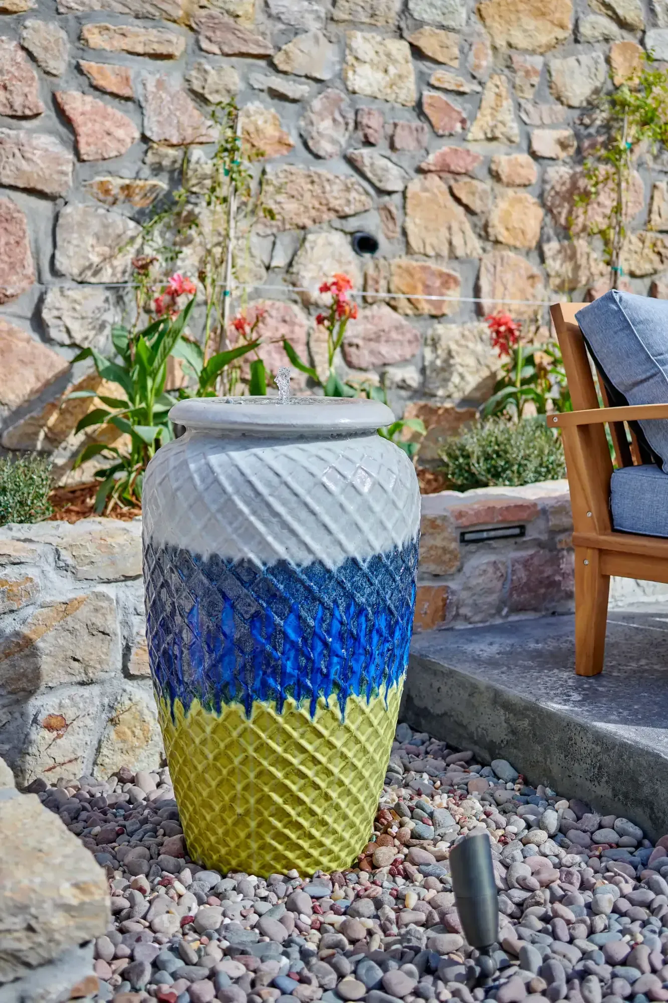 A decorative ceramic planter with blue, white, and yellow textured bands sits in a rocky outdoor setting.