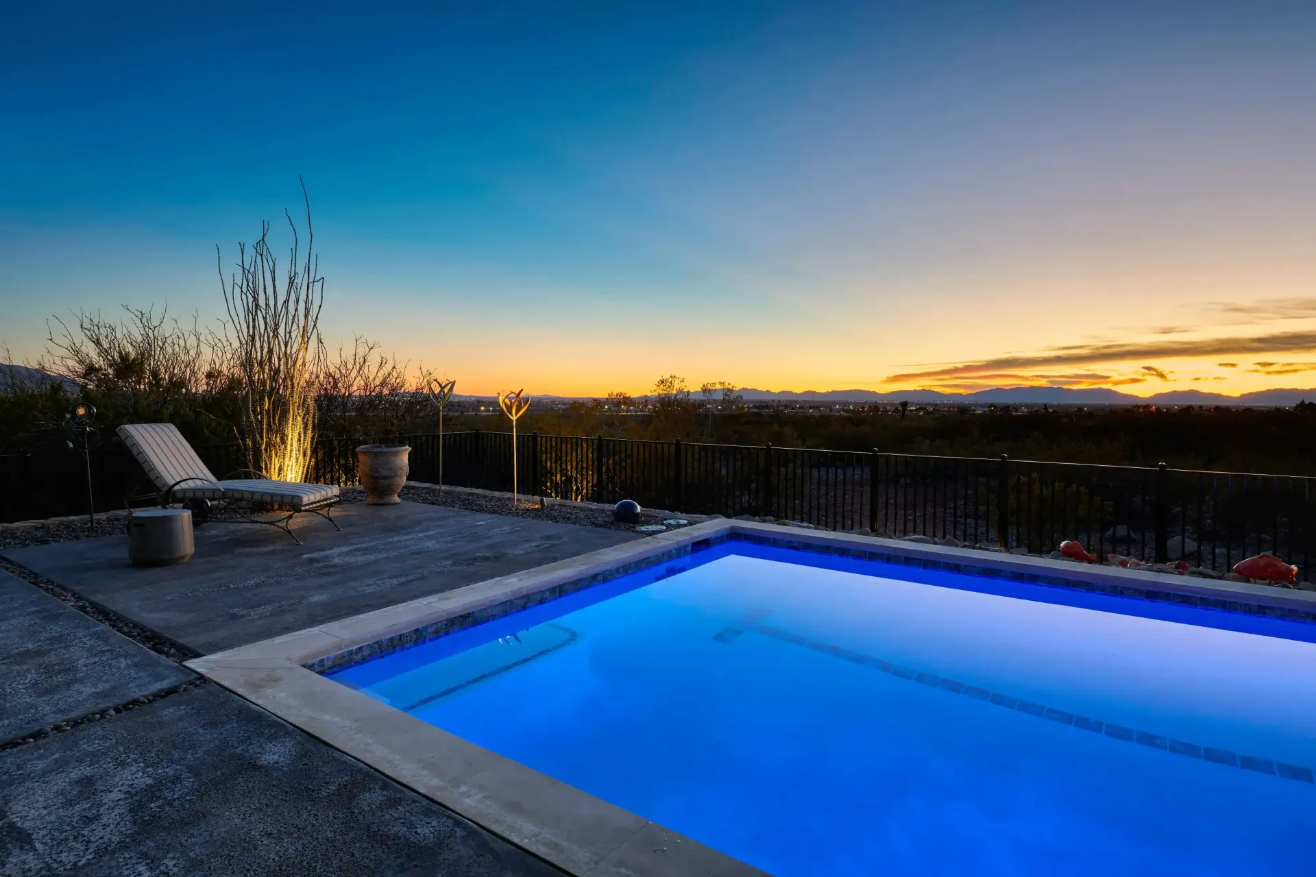 Pool at dusk with blue water, lounge chair, and a view of the sunset.