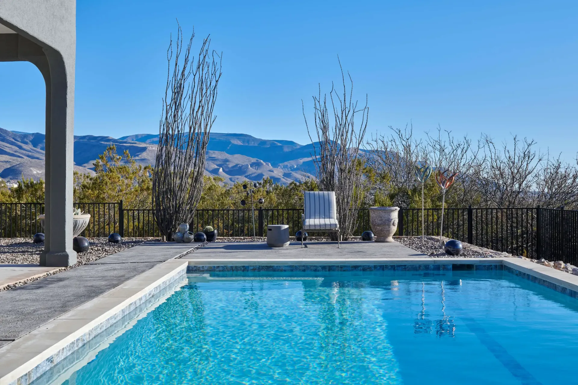 Poolside view with clear blue water, a chair, and mountains in the background under a clear sky.