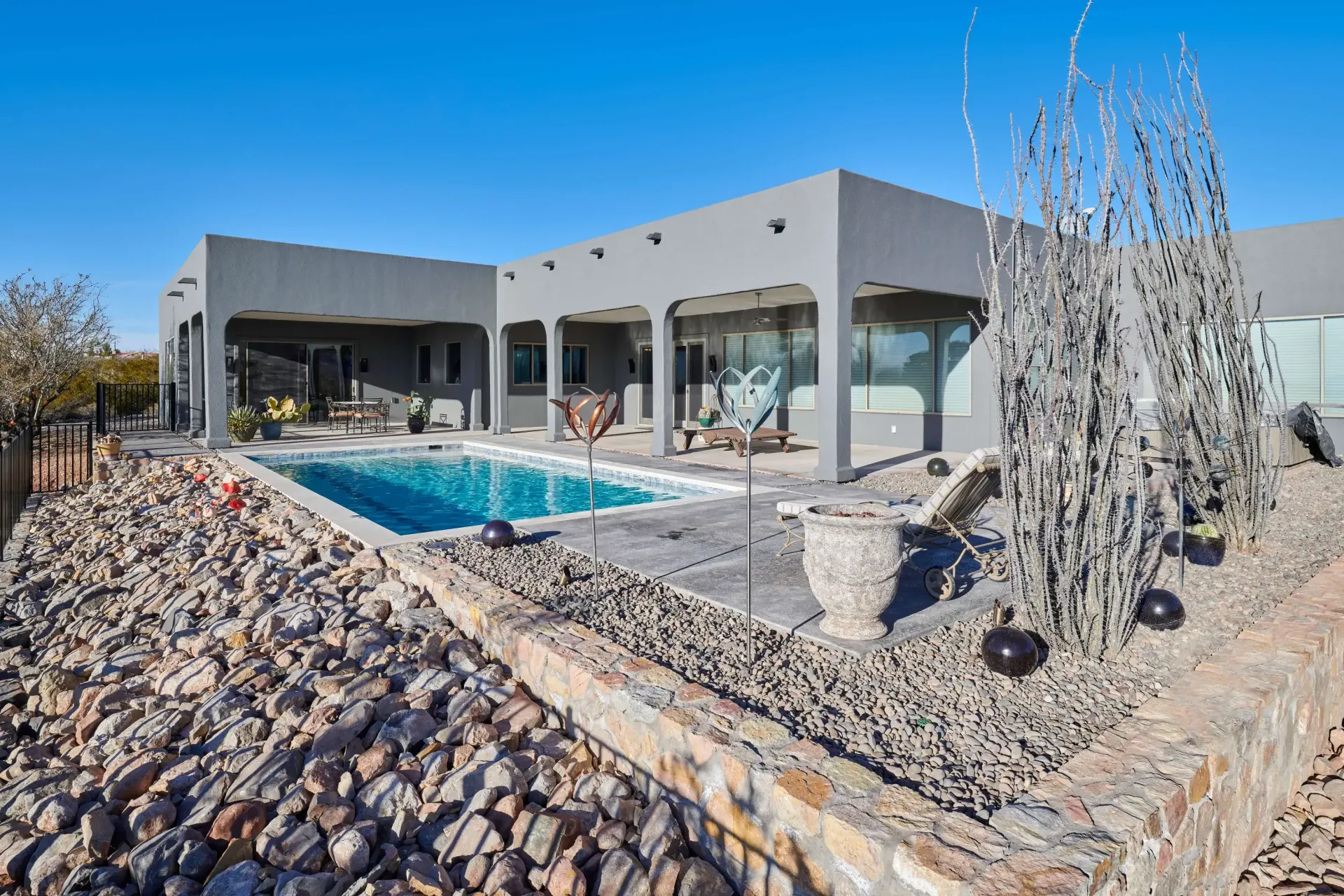 Gray stucco house with pool, patio, and desert landscaping under a blue sky.