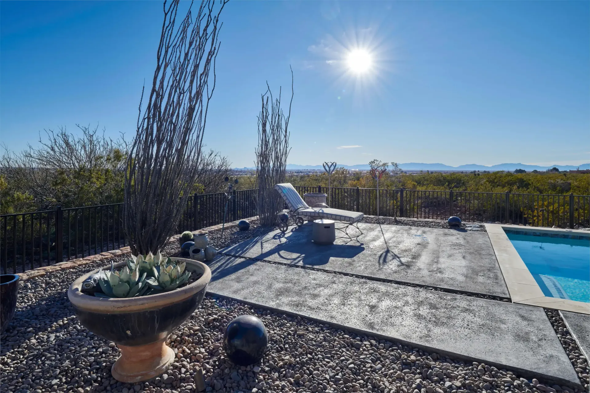 Sunny outdoor patio with pool, lounge chair, and a view of trees and distant mountains.