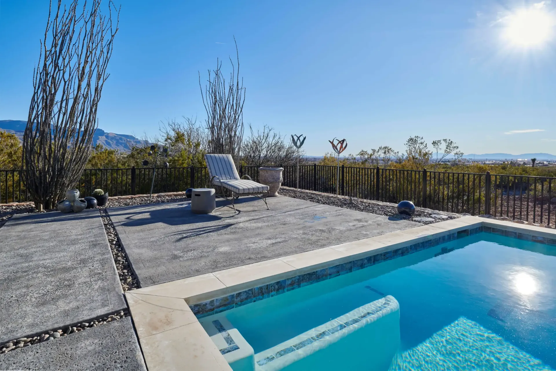 Poolside view with lounge chair, blue water, and desert landscape under a sunny sky.